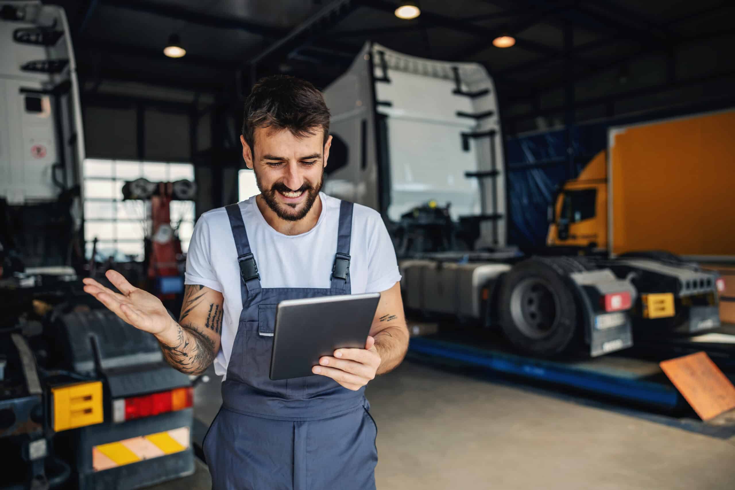 A smiling maintenance technician holding a tablet with two units on lifts in the background. Fleet Maintenance issues